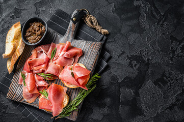 Toast with tomatoes and cured Slices of jamon serrano ham, prosciutto crudo parma on wooden board...