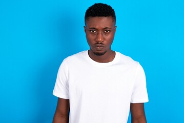 Obraz premium Offended dissatisfied young handsome man wearing white T-shirt over blue background with moody displeased expression at camera being disappointed by something
