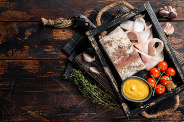 Smoked lard, slices with salt, garlic and pepper in wooden tray with herbs. Wooden background. Top view. Copy space - obrazy, fototapety, plakaty