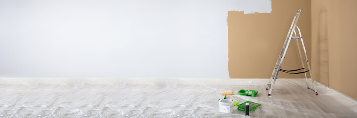 Half Painted White Wall With Ladder And Painting Equipments