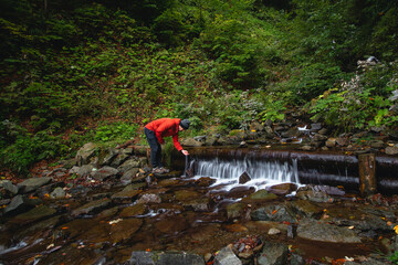 Hiker on a long trail refills drinking water from a mountain spring into a glass container. Replenishing clean water for cooking and drinking while hiking in the wilderness