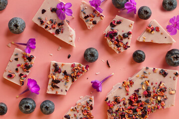 crushed pink chocolate with blueberries and flowers. Broken bars with nuts and sublimated raspberry