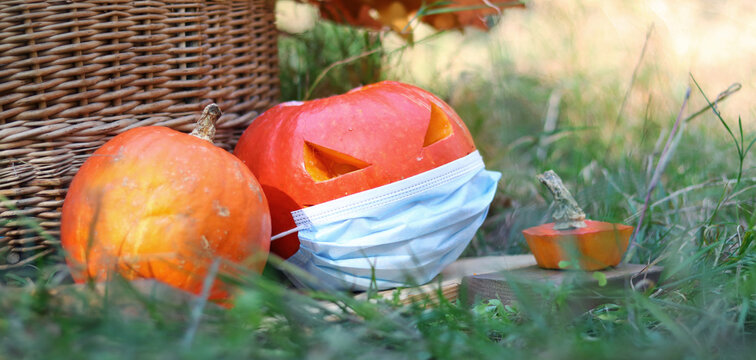 A Ripe Pumpkin With A Carved Face And Wearing A Blue Medical Mask. Halloween And Coronovirus Concept. Pumpkin In A Mask In Nature. Celebrate Safely