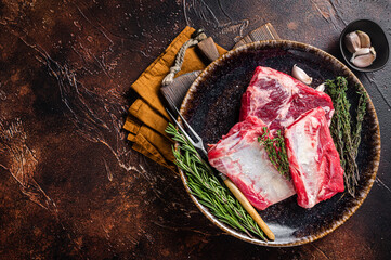 Uncooked Raw veal Short Ribs on rustic plate with rosemary. Dark background. Top view. Copy space