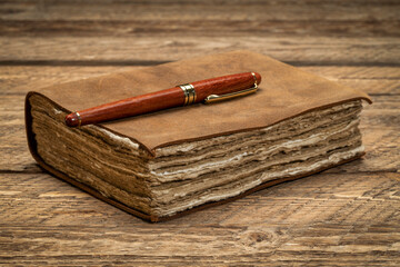 antique leather-bound journal with decked edge handmade paper pages and a stylish pen on a rustic...