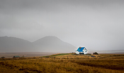 A small colourful blue house in a valley surrounded by mountains in Iceland