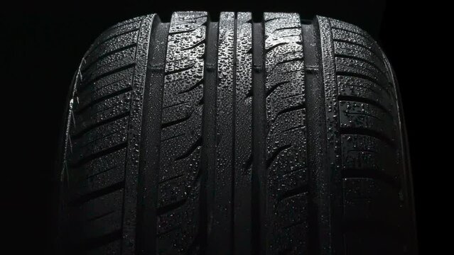 Car Tire in Water Drops. The surface of a car tire covered with shiny water drops slowly floats in front of the camera close-up