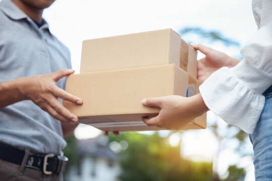 A man in a gray shirt delivers to a woman in a white shirt. The customer receives the mailbox from the delivery person in front of the condo. Freight, online shopping. and logistics concepts