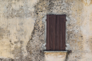 Old weathered stone wall with window and brown wooden shutter, 