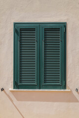 Stone wall with window and closed wooden shutter in green, vertical format