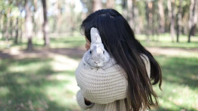 A young smiling woman holds a rabbit. Asian woman wear warm sweater with pet in relax and calm.