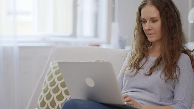 Woman at home, sitting on couch in living room, working with laptop computer Entrepreneur in home office. Portrait of happy adult caucasian woman in 30s, smiling.