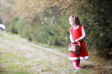 A little girl in a red hat and dresses is walking in the park. Cosplay for the fairytale hero 