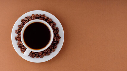 Coffee cup on a brown background. Cup of black coffee on a white saucer. Top view. Copy space