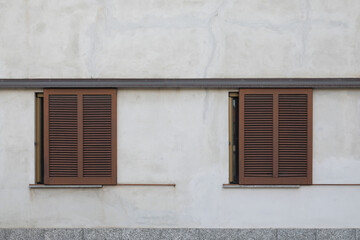 Two old and brown wooden window with closed shutters,
grey house wall with rough surface, no person