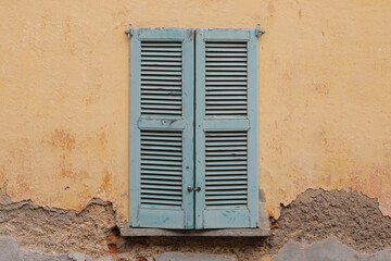 Fototapeta na wymiar old wooden window on the wall of a house, closed shutter and damaged wall with cracked surface, 