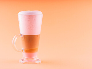 Latte macchiato coffee in glass. Latte macchiato with pink foam on coral background. Coffee drink with milk. Copy space