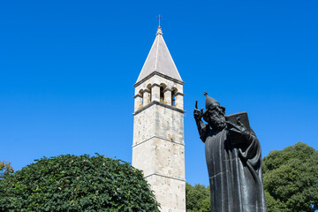 The Grgur Ninski (Gregory of Nin) statue in Split, Dalmatia, Croatia. With behind the statue the bell tower and the chapel of the holy arnir.