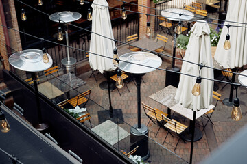 Outdoor dining tables at a restaurant with string lights hanging above located in a shopping plaza.  