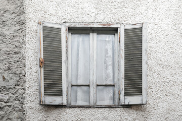 Fototapeta na wymiar Window with closed green damaged wooden shutters, painted house wall with rough and cracked surface, no person, vertical format