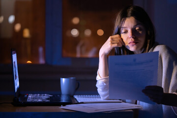 Girl is working on a laptop at night at home.