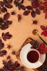 Autumn background. Autumn flat lay: a cup of tea on a wooden board and fallen red leaves on a beige background. Vertical photo. Top view. Copy space. Place for text.