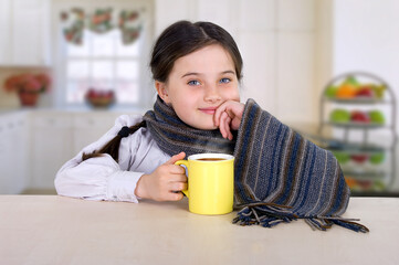 little girl drinking from a cup of hot drink tea in cold weather, sitting at home in the kitchen at the table