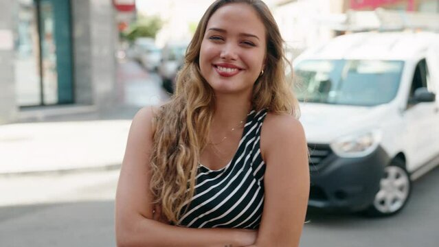 Young beautiful hispanic woman standing with arms crossed gesture at street