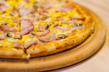 Delicious fresh pizza with ham, mushrooms and corn on a wooden tray and table in a cafe