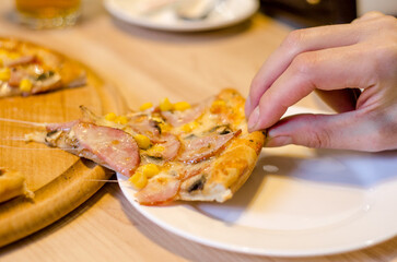 Delicious fresh pizza with ham, mushrooms and corn on a wooden tray and table in a cafe, a piece of pizza has already been eaten
