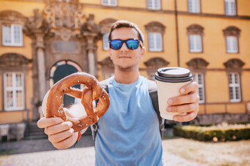 A male tourist with a pretzel and a mug of takeaway coffee on the background of an old German building. Travel and tourism