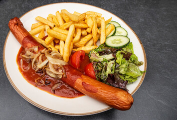 Deep-fried currywurst with French fries, salad and roasted onions