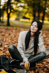 Fototapeta na wymiar Young beautiful woman with dark hair in a leather jacket walks in the park in autumn