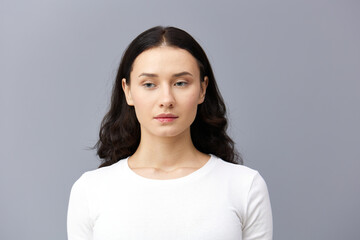 a gentle woman stands on a dark background in a tight white T-shirt, calmly lowered her hands down and looks forward