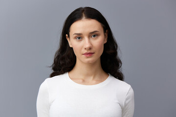 a gentle woman stands on a dark background in a tight white T-shirt, calmly lowered her hands down and looks forward