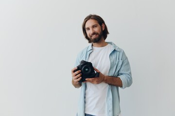 Obraz premium Man hipster photographer in a studio against a white background holding a professional camera and setting it up before shooting. Lifestyle work as a freelance photographer