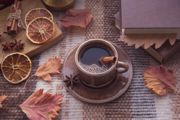 Autumn mood, autumn atmosphere. A cup of hot coffee, cinnamon sticks, star anise, a book, autumn leaves on a knitted plaid on a rainy day.