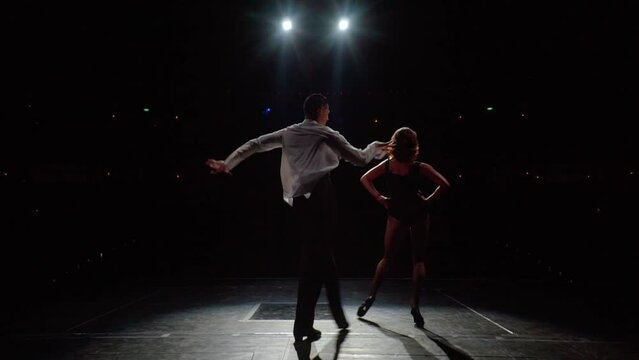 Ballroom dancers pair on concert hall stage,rear view.Slow motion synchronous dance movements and ballroom steps with hip swinging,arm swings,bends.Expressive couple dance fragment.Black and white .