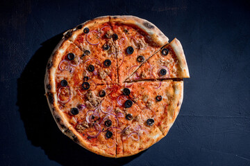 Pizza with tuna, olives, onions, mozzarella cheese and tomato sauce on a black background. Top view