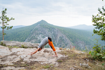 Dog face down pose, young guy practices yoga in the mountains, training of inner strength of spirit, gymnastics for joints, triangle mountain
