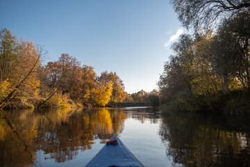Autumn landscape. The nose of the kayak against the backdrop of the lake. Yellow trees on the bank of a forest river at sunset. Landscape in warm colors of sunlight