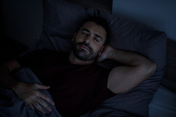 Top view of a handsome bearded man sleeping comfortably at night on the bed in his bedroom.