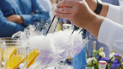 Cocktail bar with bartender working on summer party outdoors. Glasses with colorful drinks stand on bar counter. Unrecognizable man puts straw in wineglass. Celebration, festival