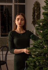 Young woman in dress poses near Christmas tree. Selective focus. Images for articles about Christmas, holidays.