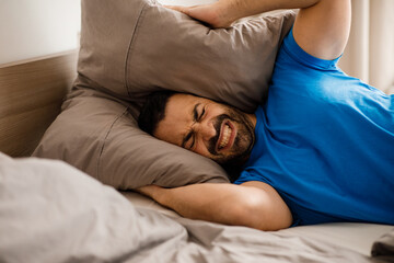 A young arab man holds a pillow with two hands covering his ears from the loud noise at home, a sleepless night, close-up with free space