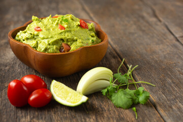 Fresh guacamole with tomato lime and coriander in a wooden bowl