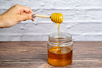 Honey drizzling. Pot of honey and wooden stick isolated white brick wall