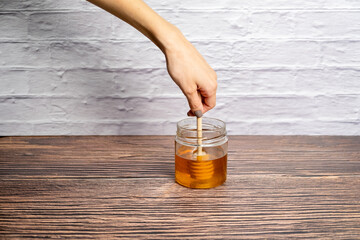 Pot of honey and wooden stick isolated white brick wall