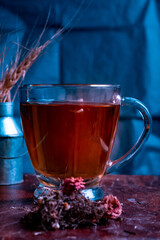 Té de hiervas rojo en taza de cristal con fondo negro con textura rugosa.