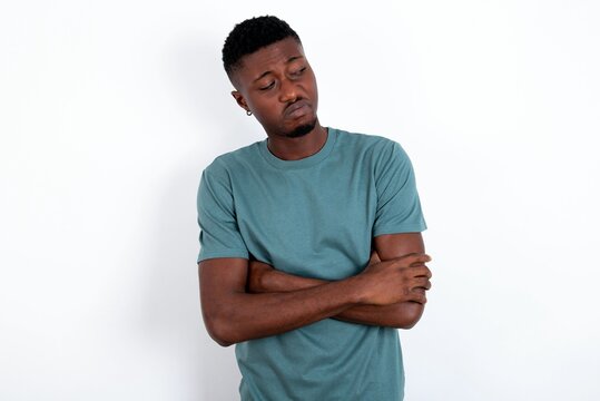 Displeased young handsome man wearing green T-shirt over white background with bad attitude, arms crossed looking sideways. Negative human emotion facial expression feelings.